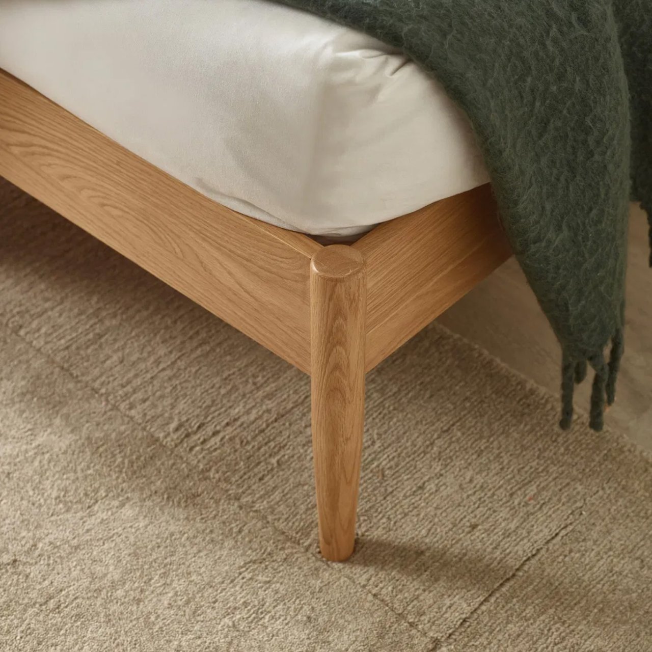 View of the front corner and the tapered wooden leg attached seamlessly to the sides of the bedframe