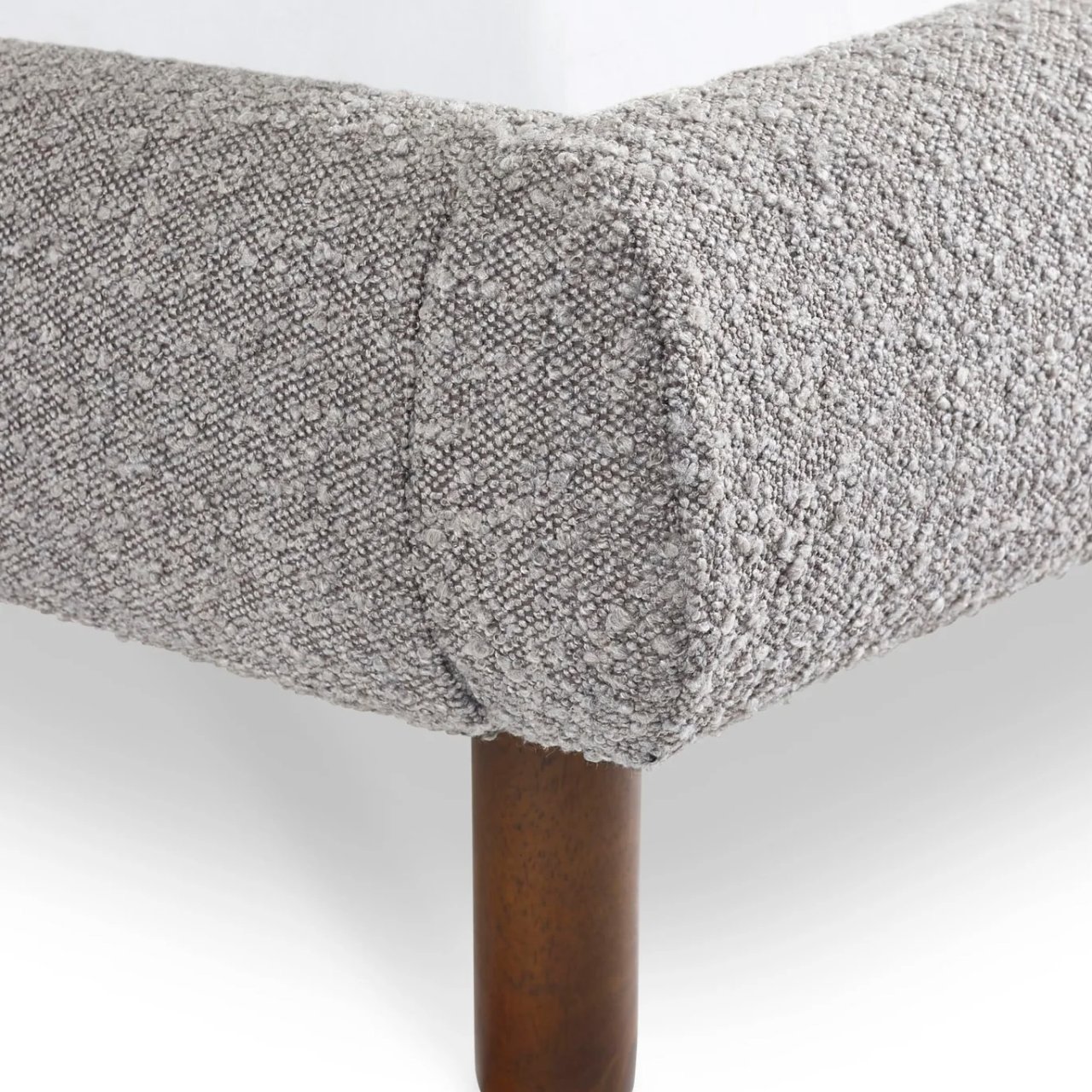 Front corner of the bed with the boucle fabric intricately stitched and the round walnut leg in full view