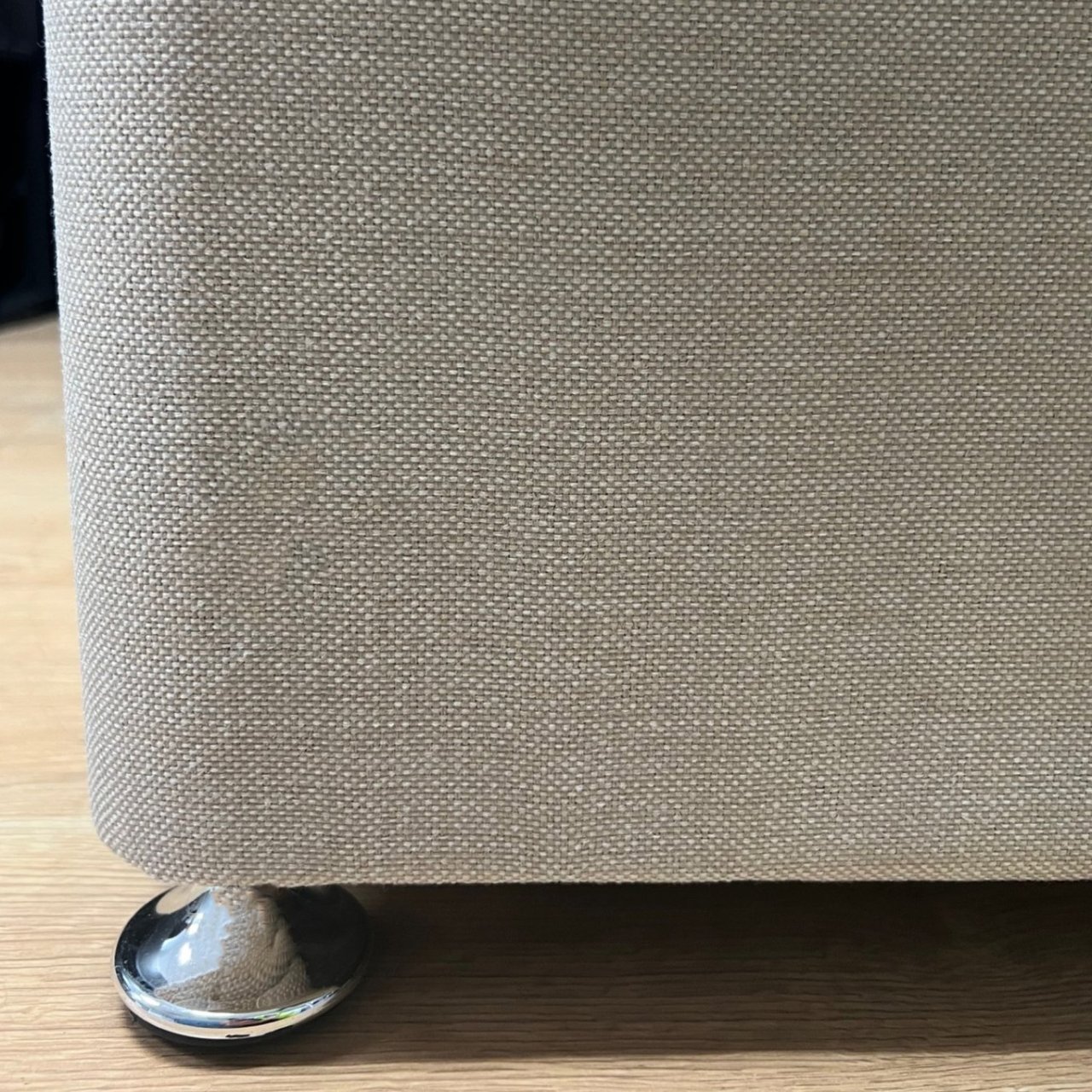 Zoom in on the light vanilla fabric and the shiny chrome glider at the bottom of the bed