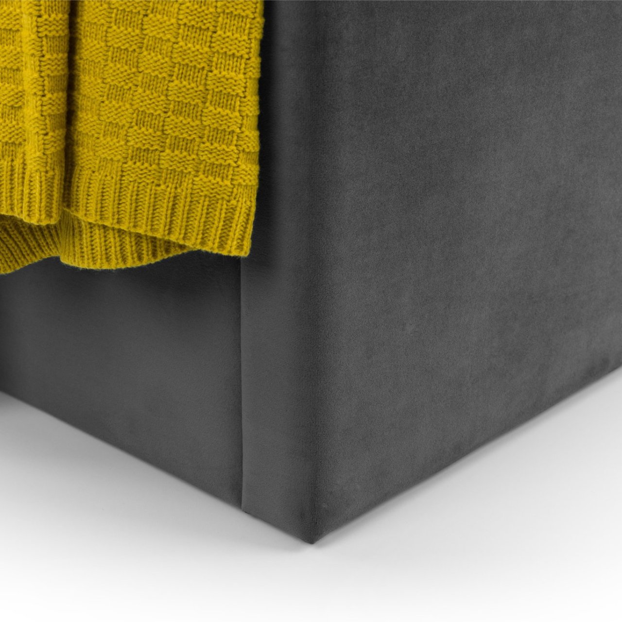 View of the corner of the bed with a yellow throw next to it revealing the complementing grey and mustard colours 