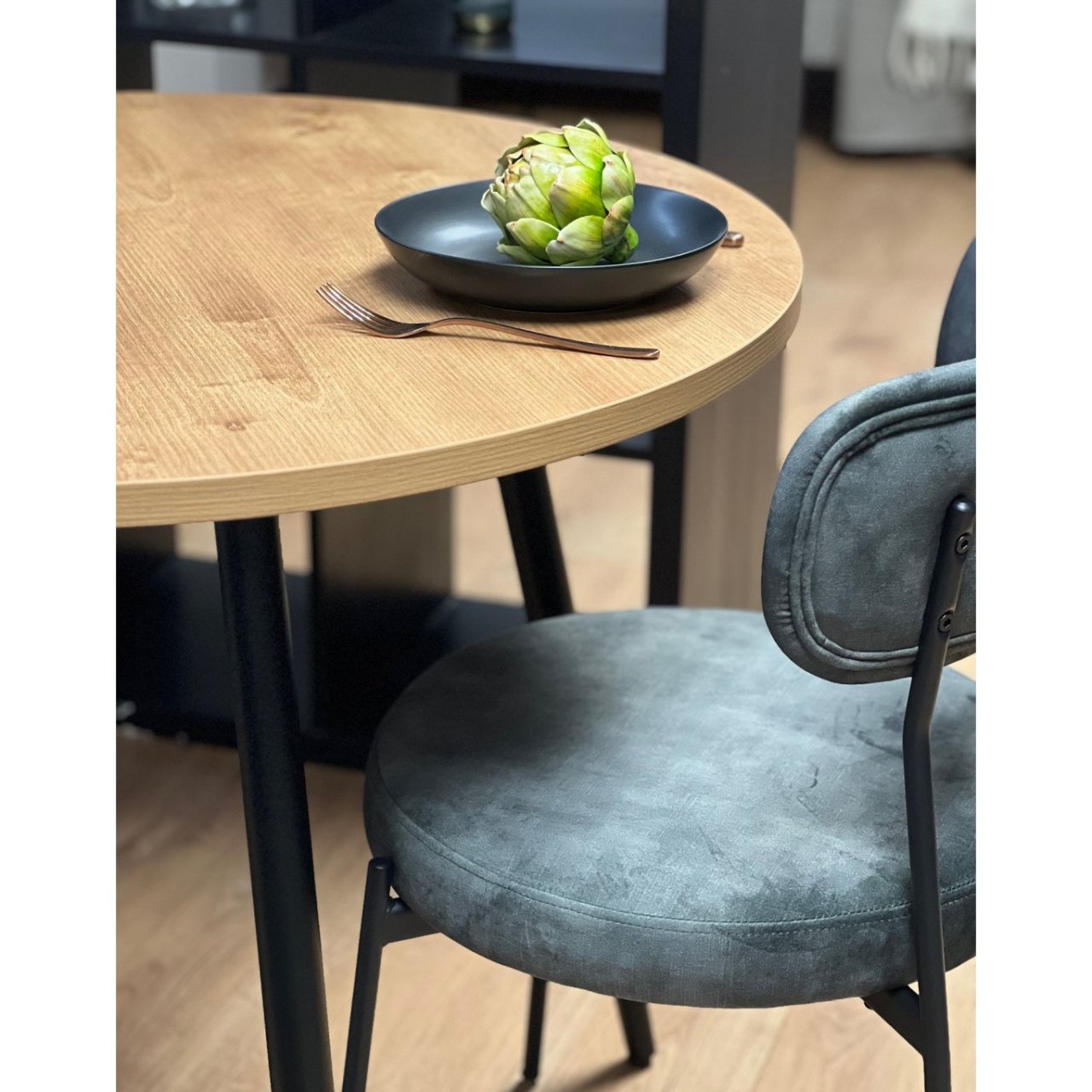 Zoomed in view of half the round dining table with oak top and a velvet dining chair next to it