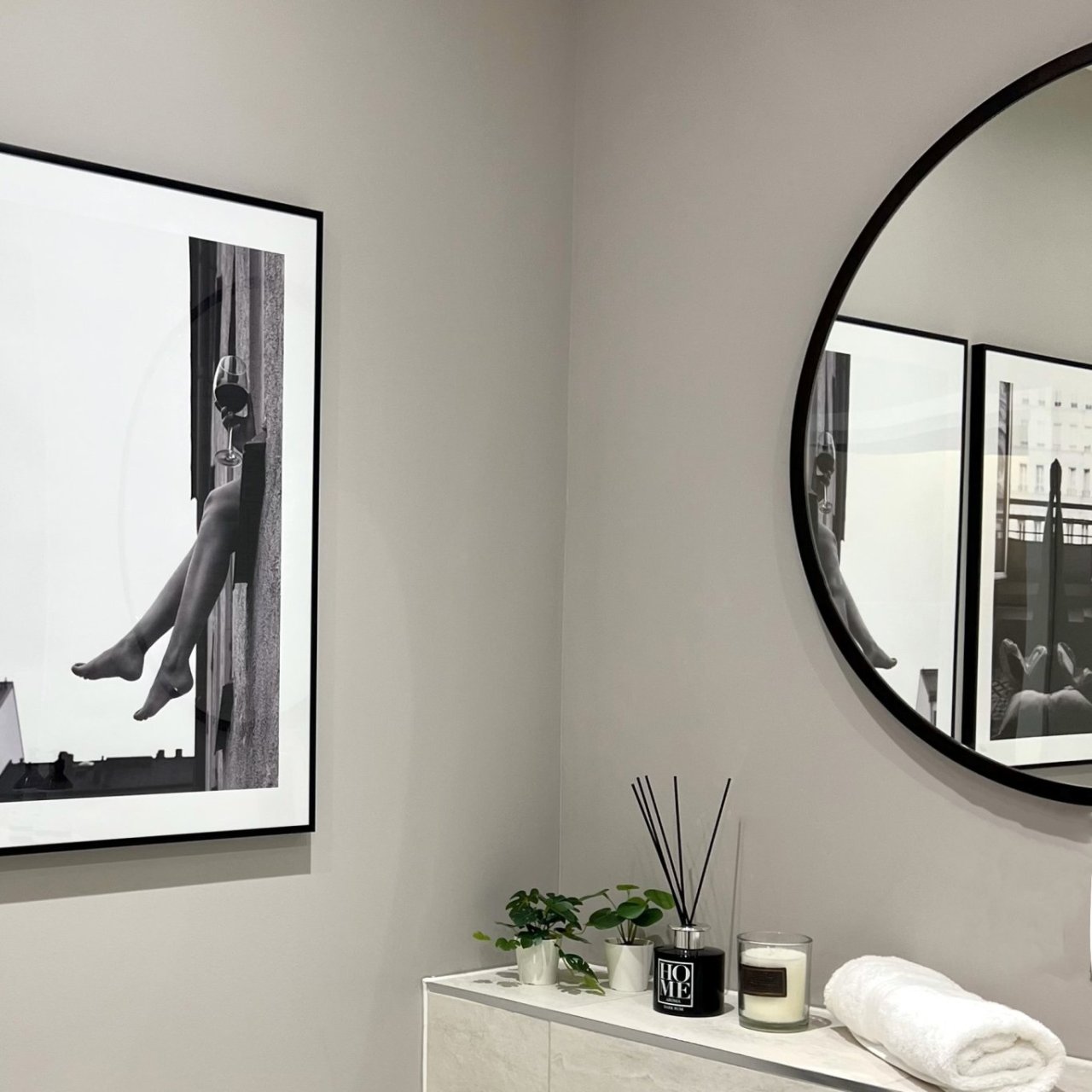 Lifestyle shot of the round mirror with black frame standing over a decorated sideboard 
