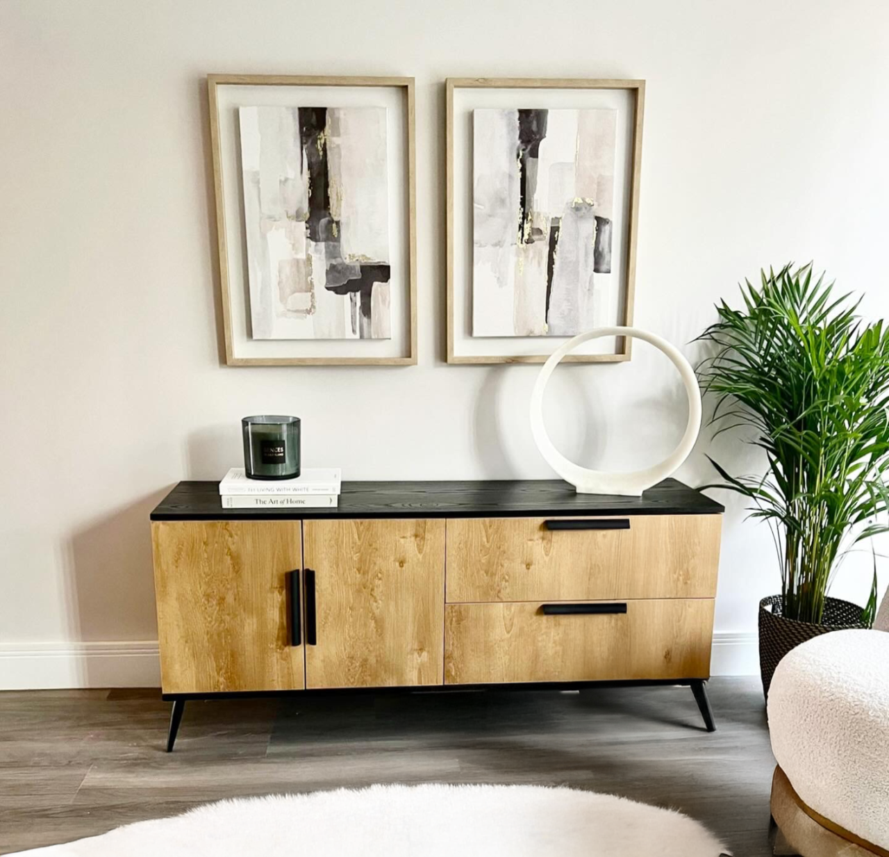 Lifestyle shot of the Elene sideboard complete with books and decorations on top of it, a pair of prints hung above and a white fluffy rug in front