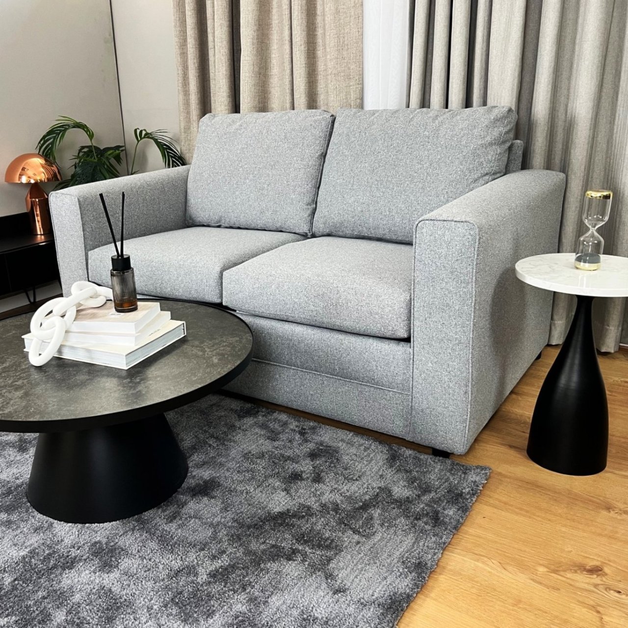 Lifestyle shot of the March 2.5 seat sofa bed in a modern setting with a round coffee table up front and a fluffy grey rug. A round marble-top side table is standing on the left hand of the sofa