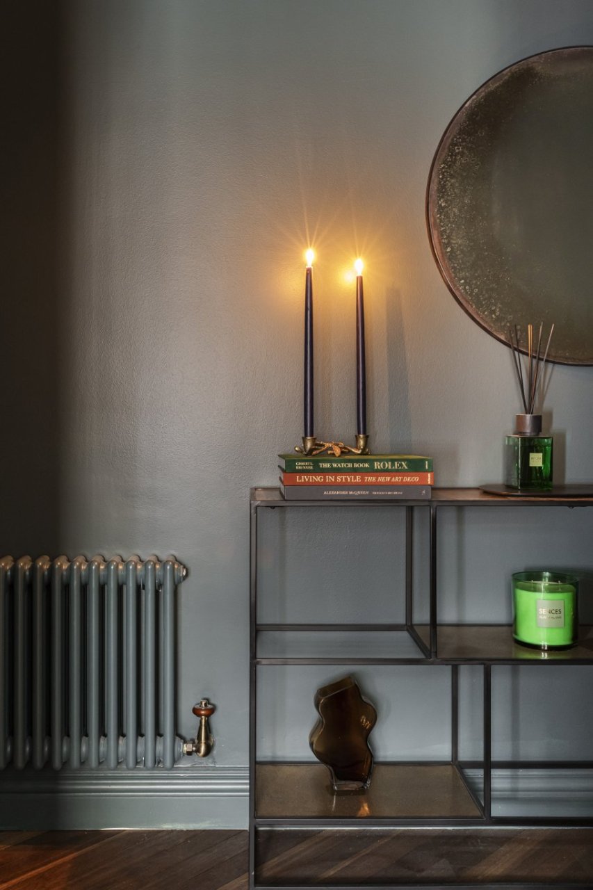 Alternative view of half the shelf showcasing style books, scented candle and diffuser and a radiator painted the same dark colour as the wall behind.