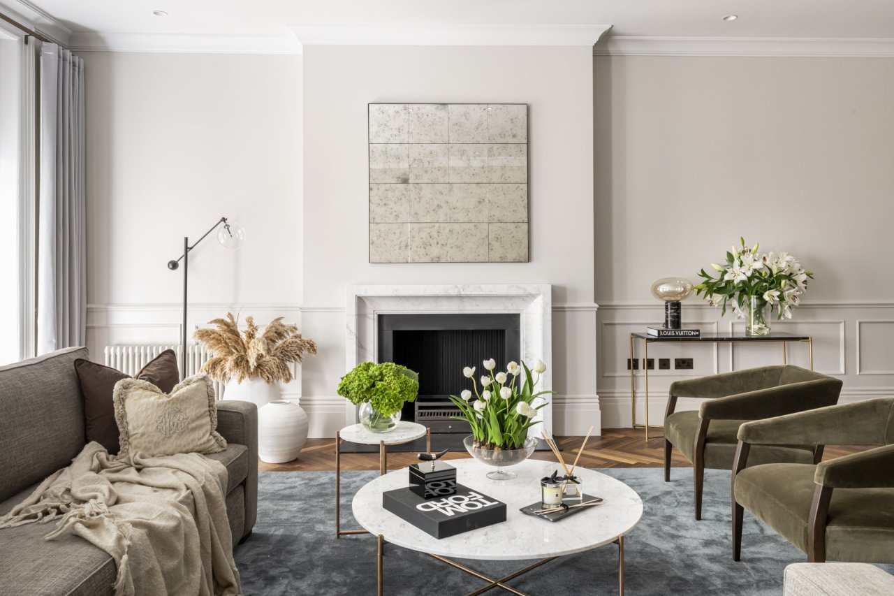 Spacious living room viewed from above a corner sofa, facing a fireplace. A professionally dressed coffee table takes centre stage with a small complementary side table beside it.