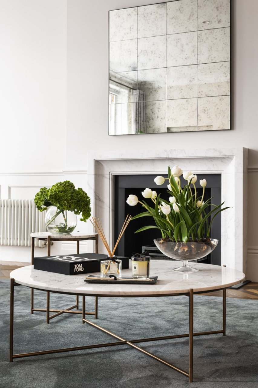 A focus on the marble and metal round coffee table with its pairing side table. They are both beautifully decorated with fresh plants, a diffuser and a Tom Ford book.