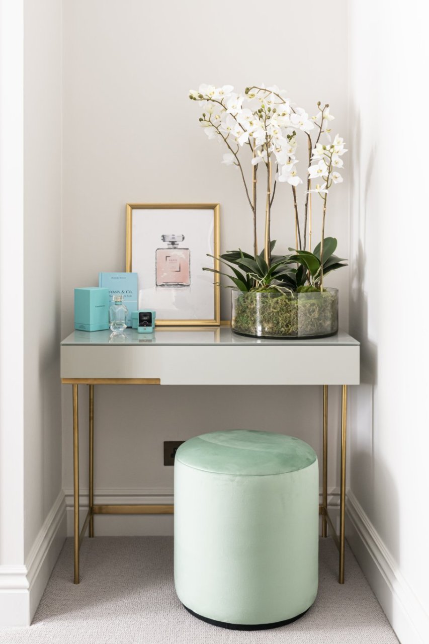 A dressing table tucked in a corner with a smooth, velvety pouffe in front of it and a selection of Tiffany & Co products on top.