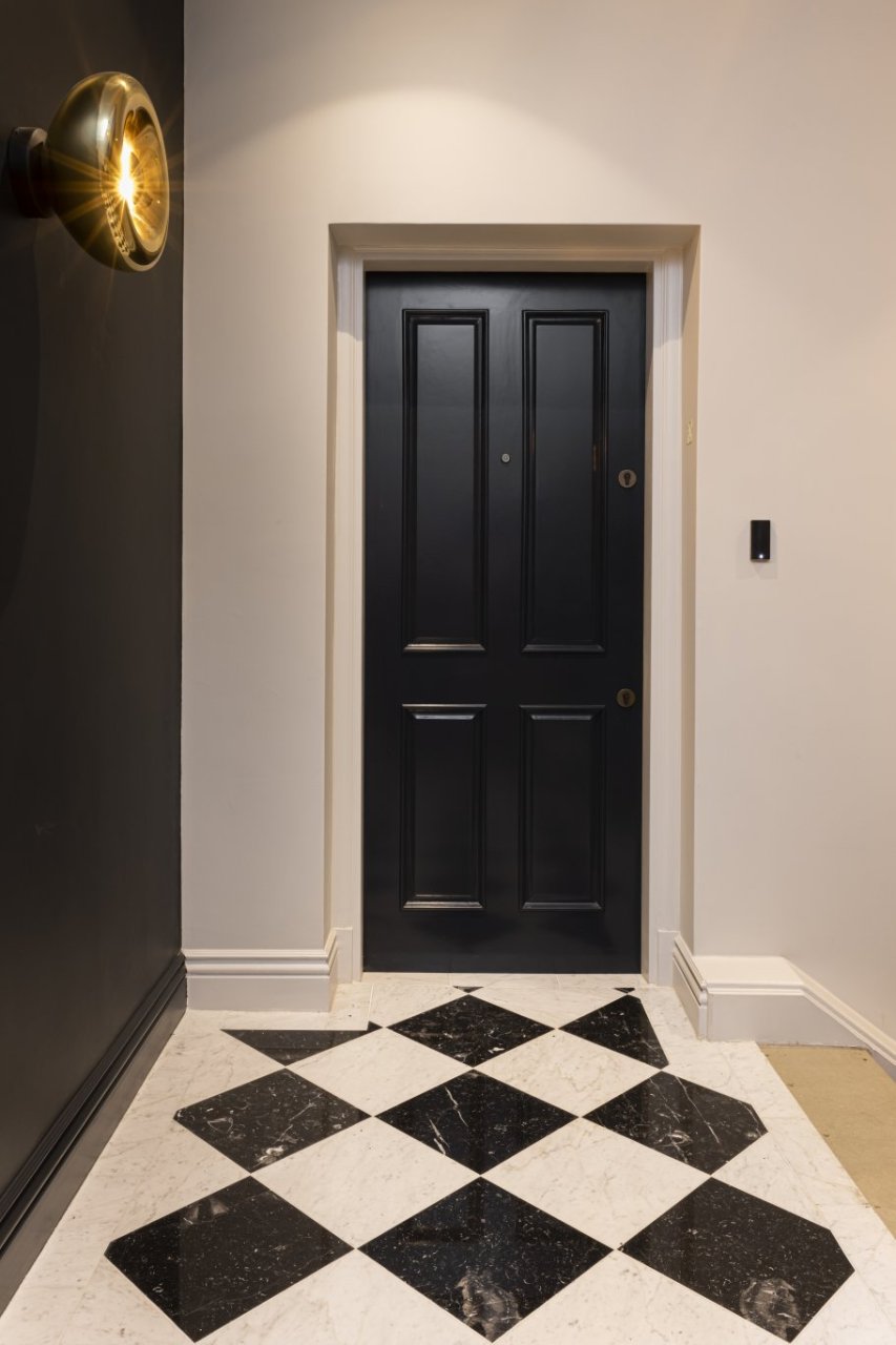 A view of the apartment from outside, showcasing a sleek dark door and a checkered marble floor of alternating black and white squares.