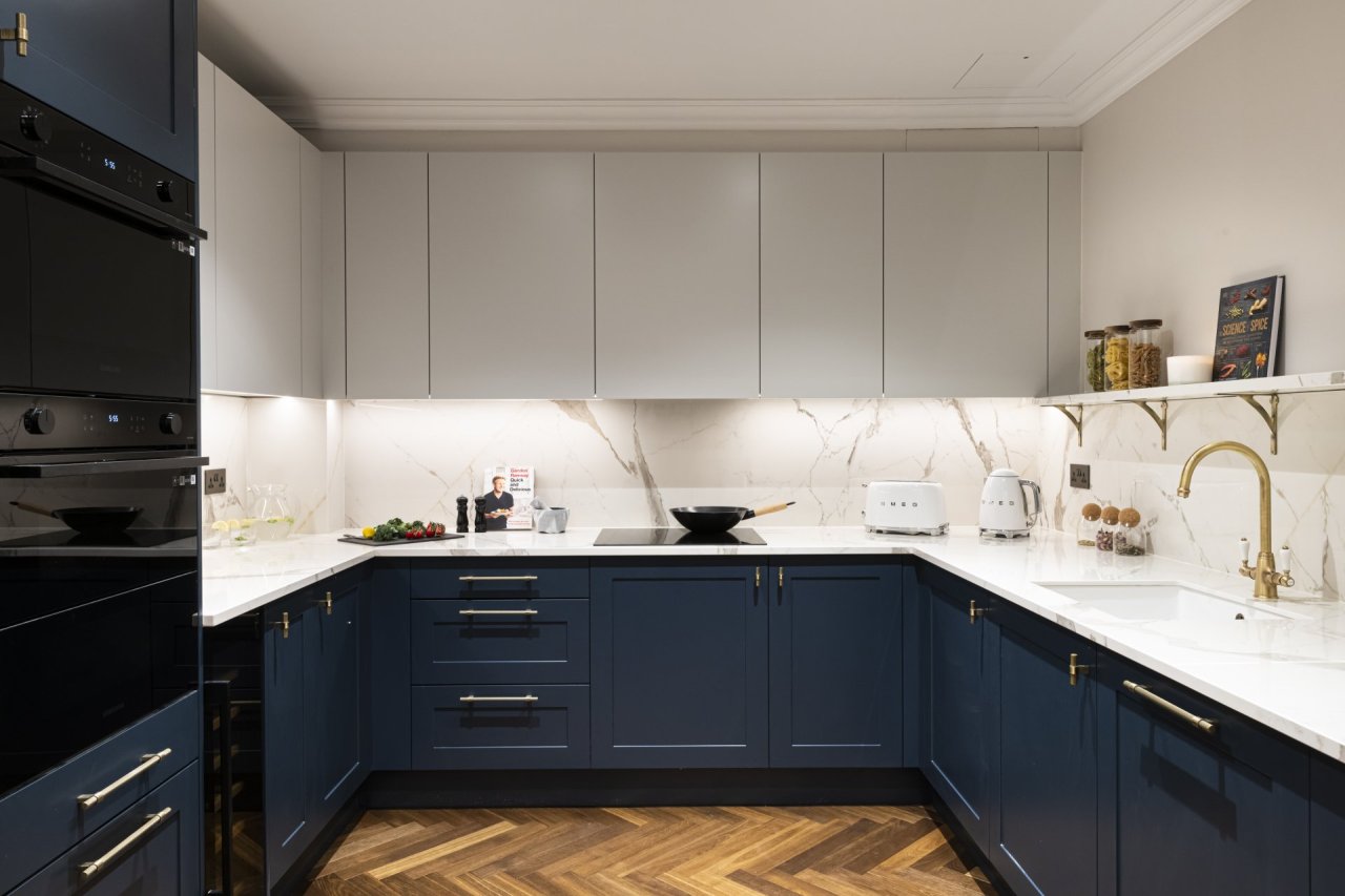 Blue and white kitchen area with marble top surfaces and sleek, black, cooking ovens. 