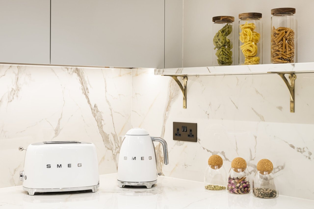 Smeg toaster and kettle sitting on a brilliant, pristine marble surface. Types of pasta are placed in elegant jars above with spices below.