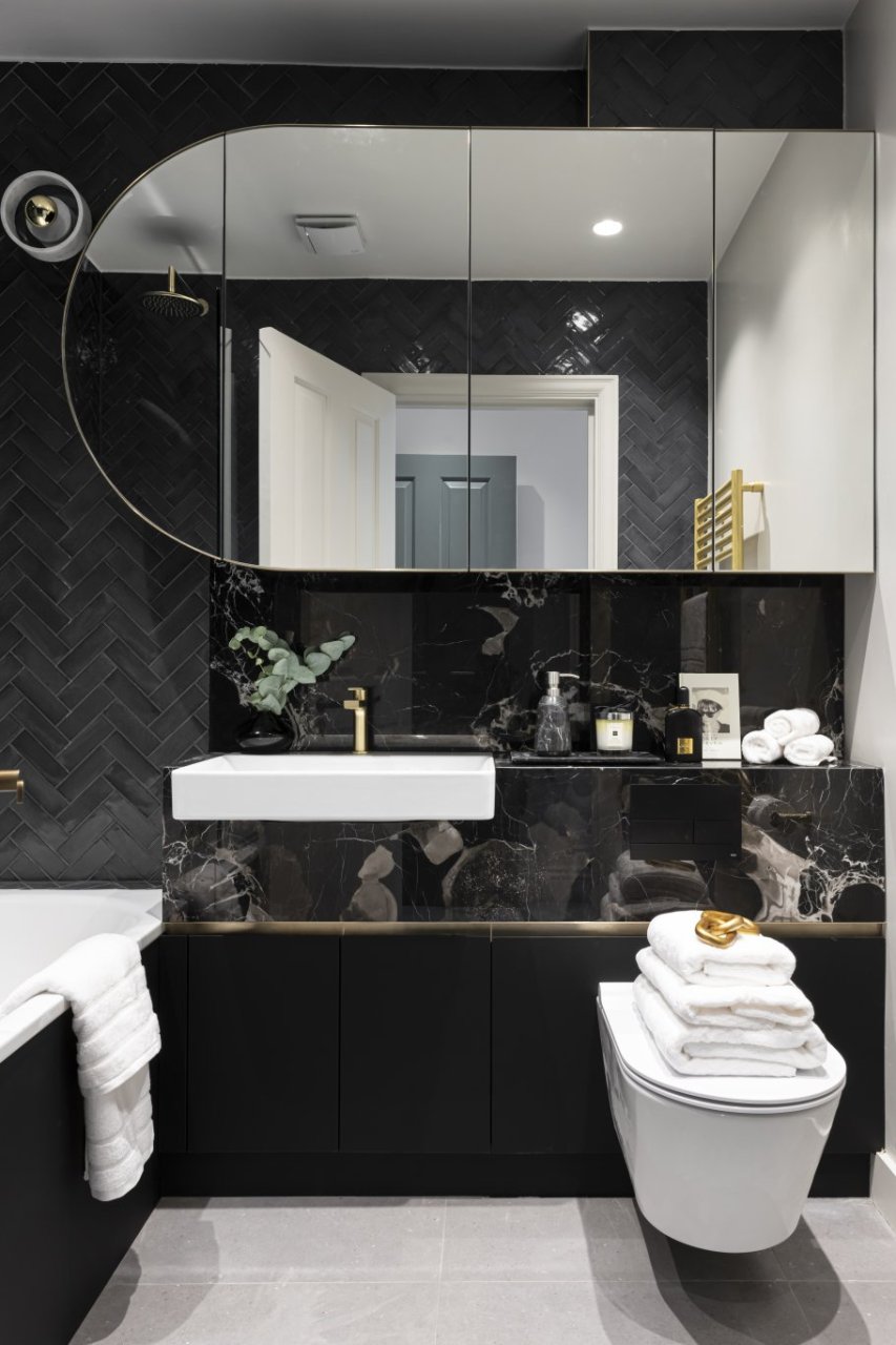 A bathroom covered in black marble and black porcelain tiles. Multiple towels for hands and showering everywhere as well as a fancy soap bottle and a cotton candle. 