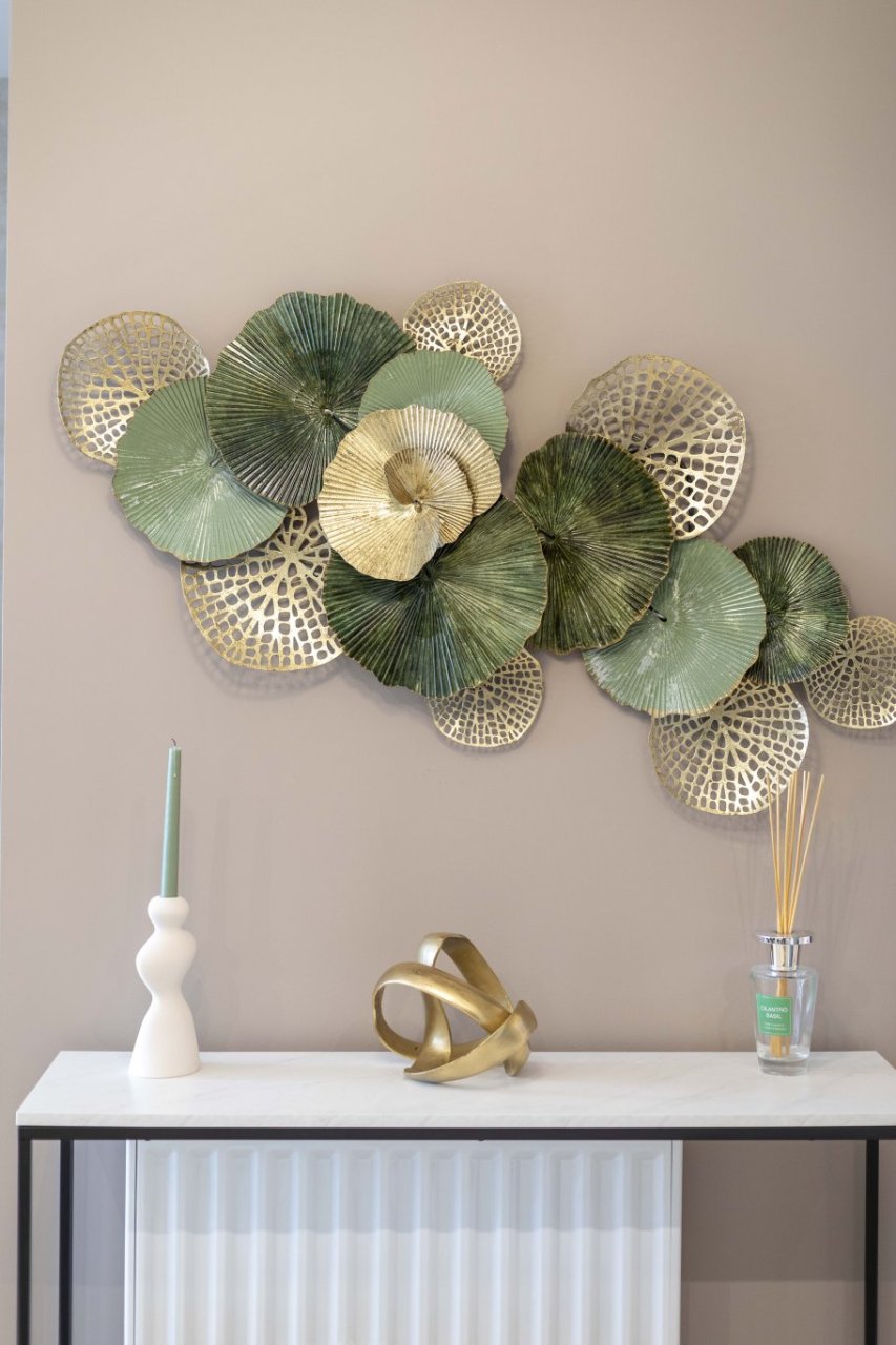 A console table with accessories on it in the form of a diffuser, candle and abstract sculpture. On the wall above it there is a beautiful sculpture of floral and web-like patterns.
