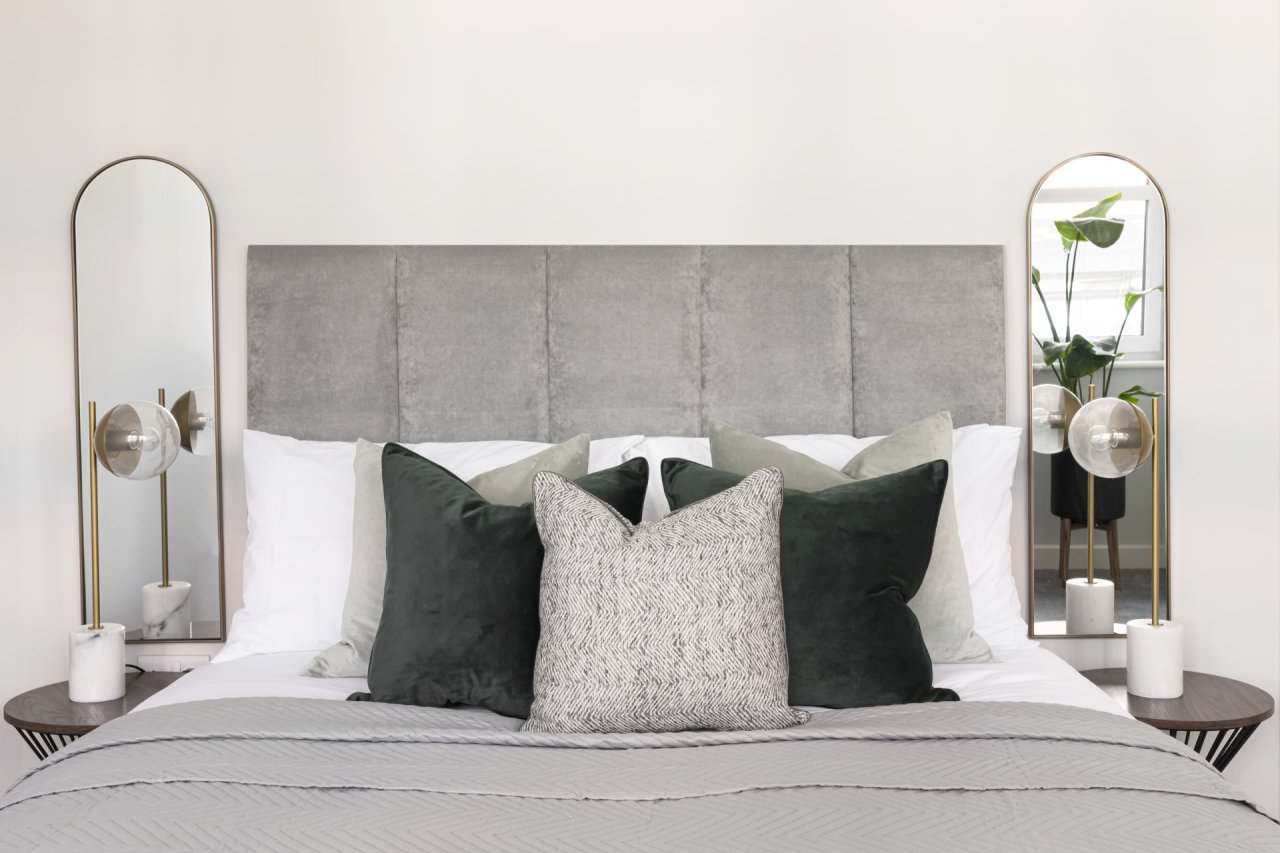 Symmetrical shot of the bed focusing on the set of scatter cushions that create a pattern on it and the towering headboard surrounded by tow bedside mirrors.