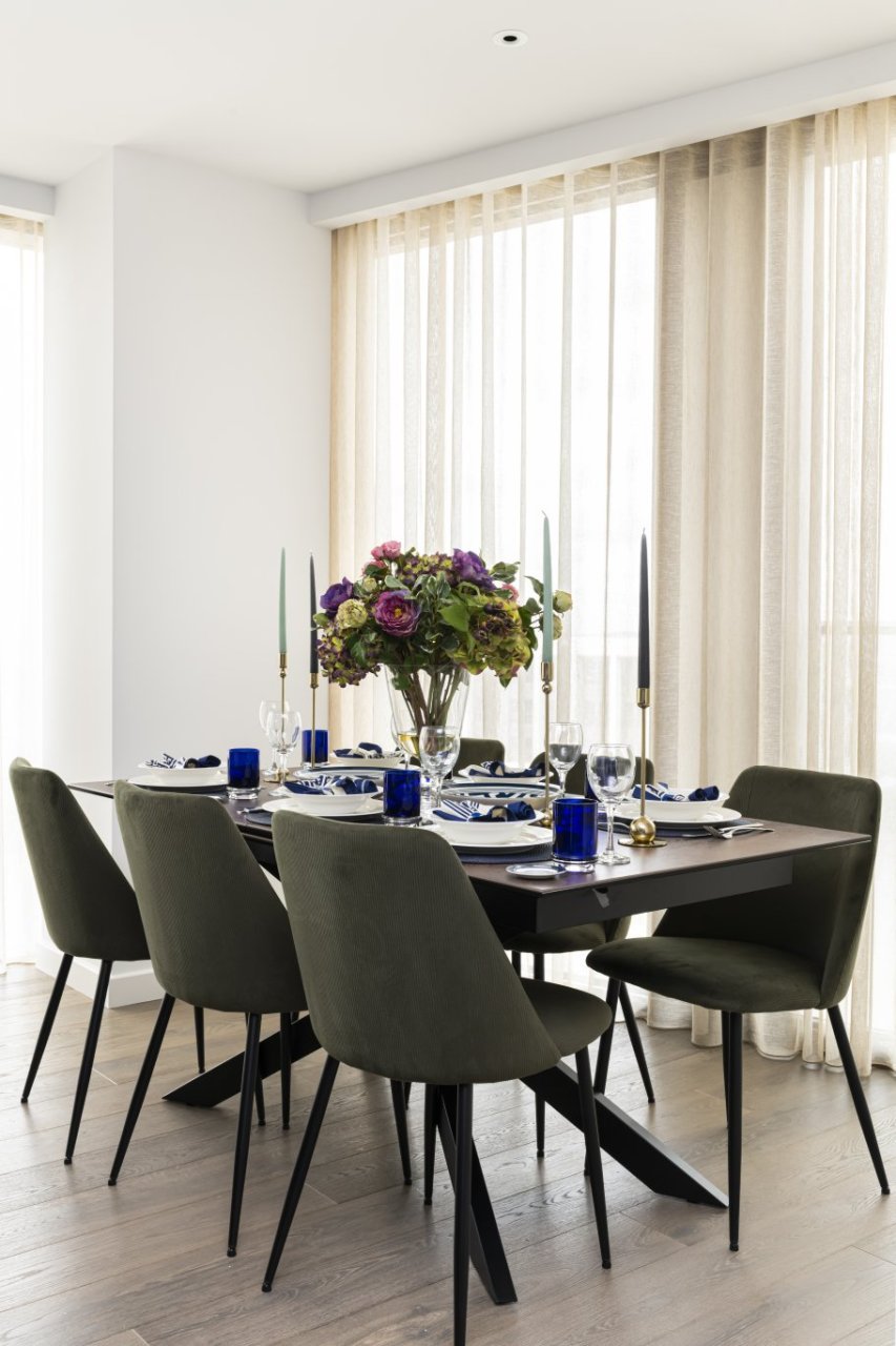The dining table in its full beauty, revealing the tapered legs that combine to a middle column and the minimalist shape of the surrounding dining chairs.