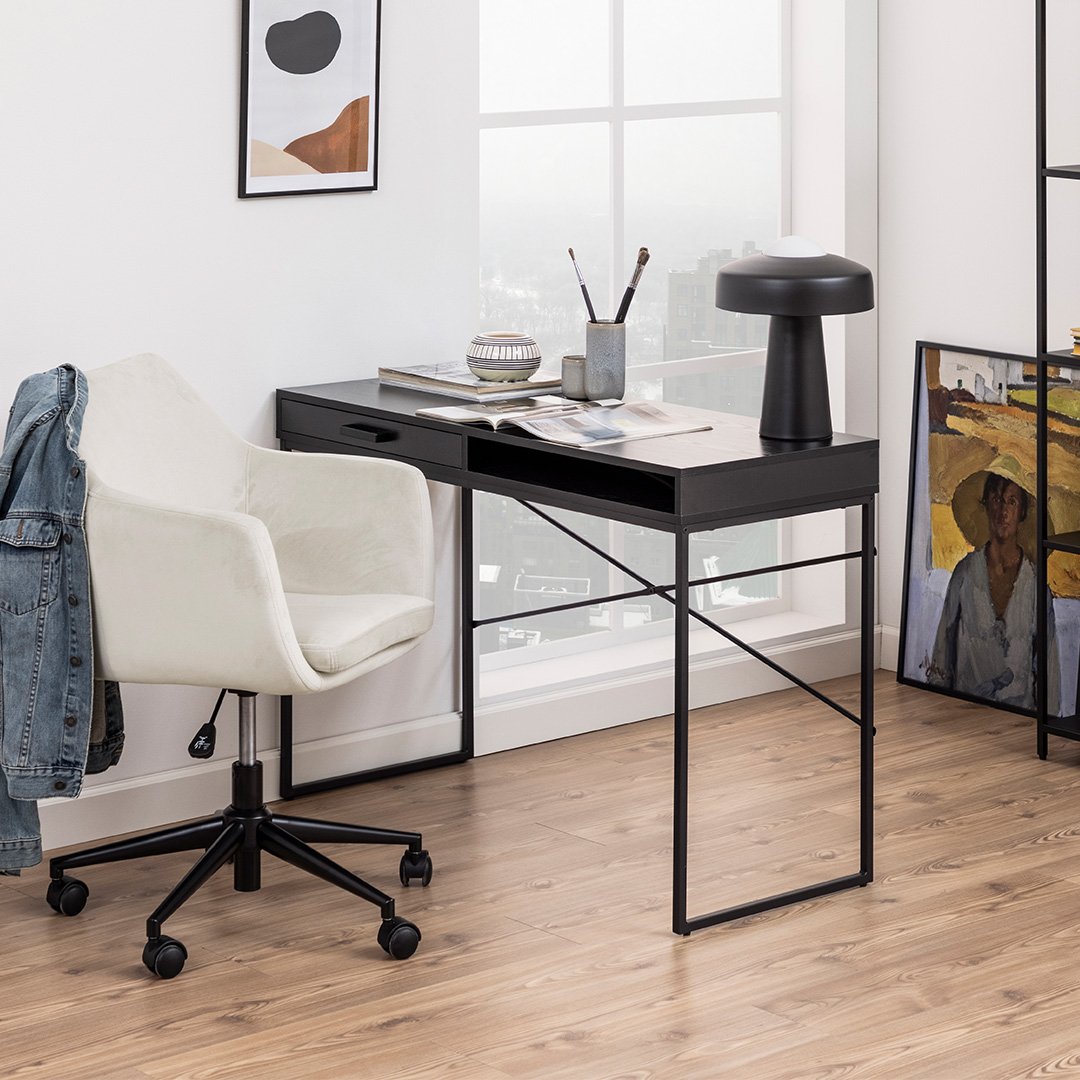 Lifestyle shot of the see black desk with books and acessories on top and a contrasting white office chair