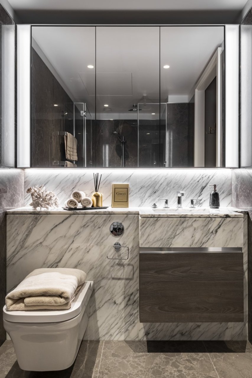 A streaky sleek marble bathroom with a whole wall mirror above the sink and a variety of towels.