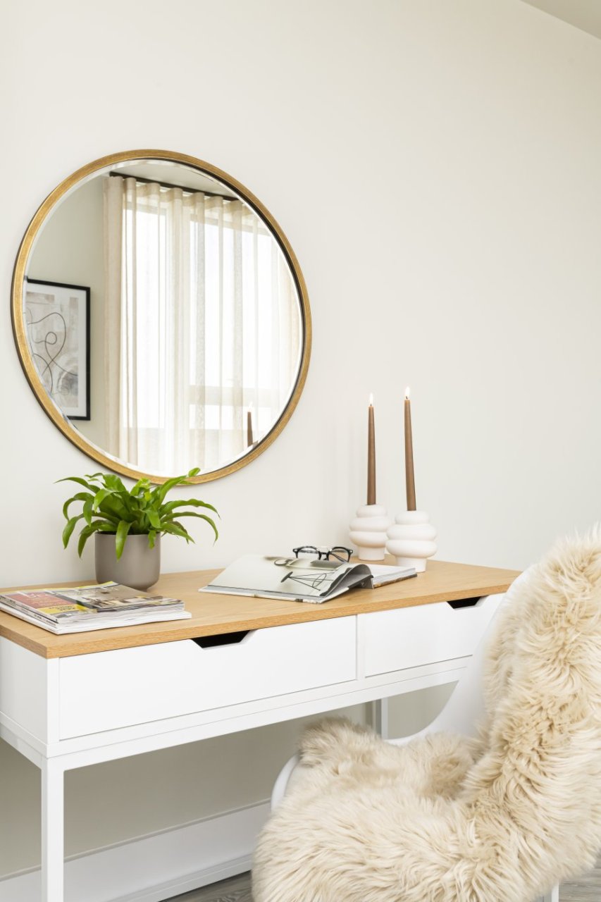 A solid, white chair covered in a fluffy throw placed in front of a dressing table with two shelves and natural accents.