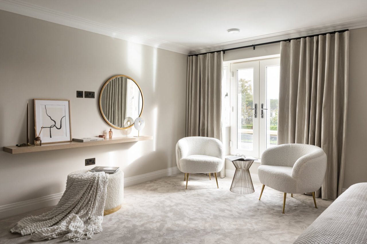 The rest of the bedroom features two woolly armchairs with a small cage side table between. On the wall, an attached surface serves as a dressing table with a sumptuous white and gold pouffe beneath it.